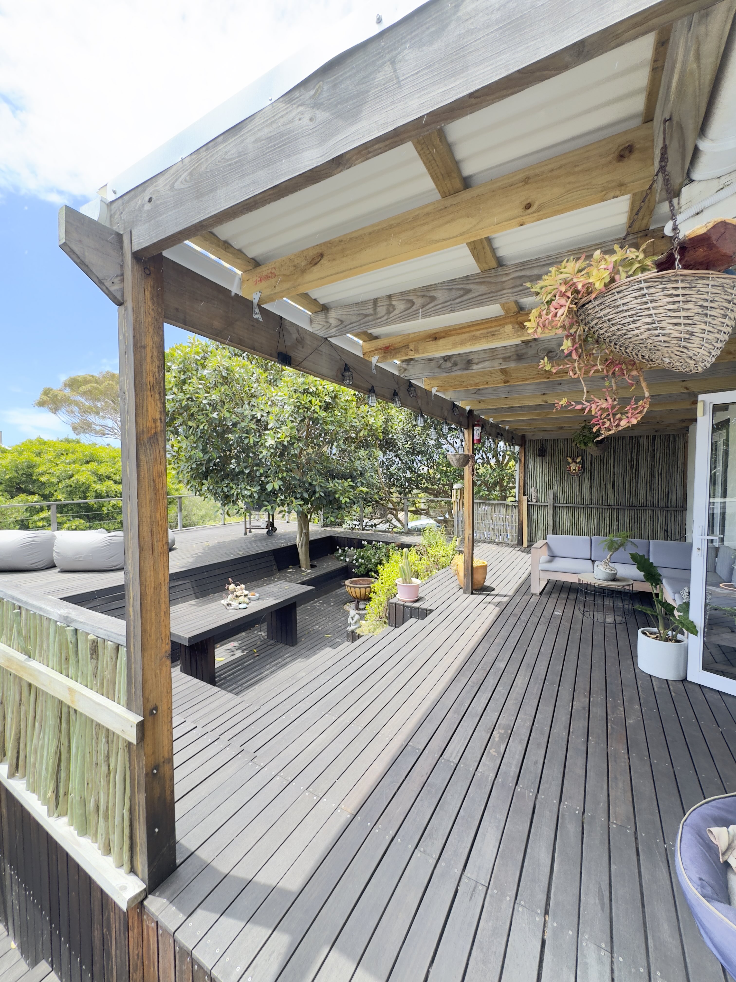 A large covered Balau deck with a timber pergola, built in bench seating and a lounge opening to the garden