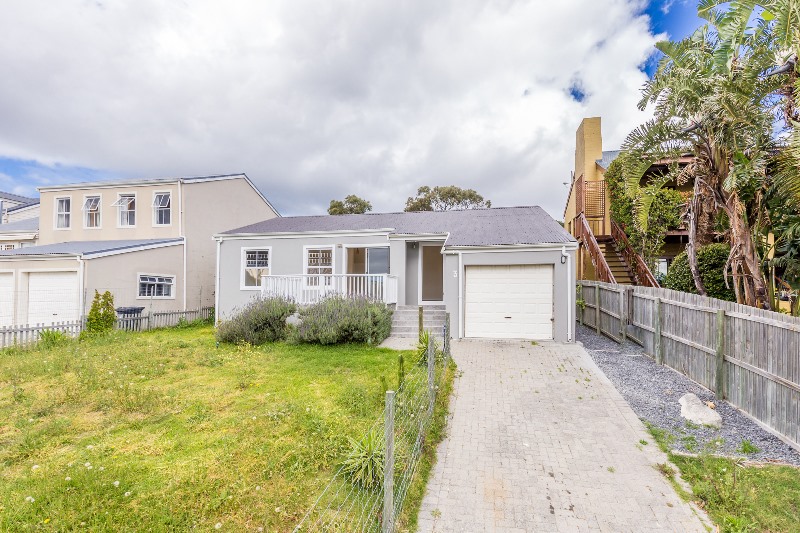 The original grey plastered house from the front with a covered porch, single garage and an overgrown lawn