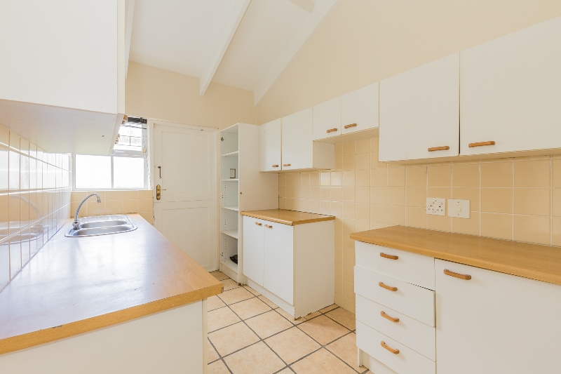 The original kitchen with white melamine cabinets, laminate counters and cream wall and floor tiles