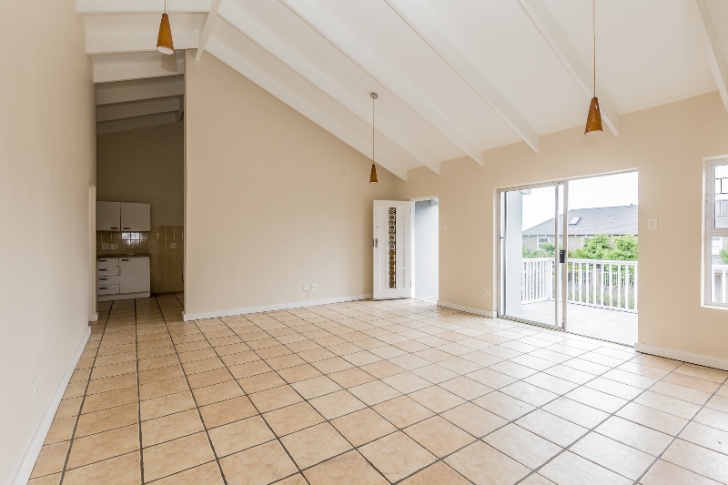 The empty open plan living and dining room with a vaulted beamed ceiling and sliding doors to a railed balcony