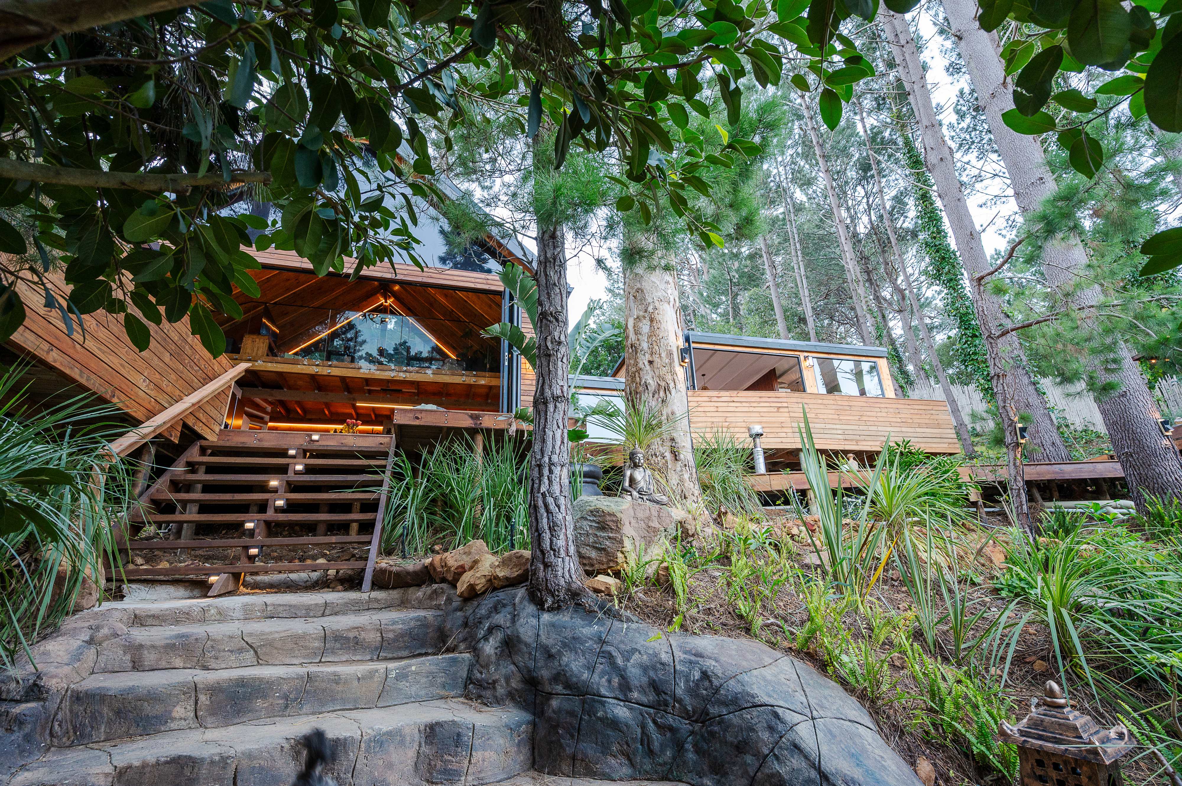 A timber home with a glass gable glowing among tall pines at dusk