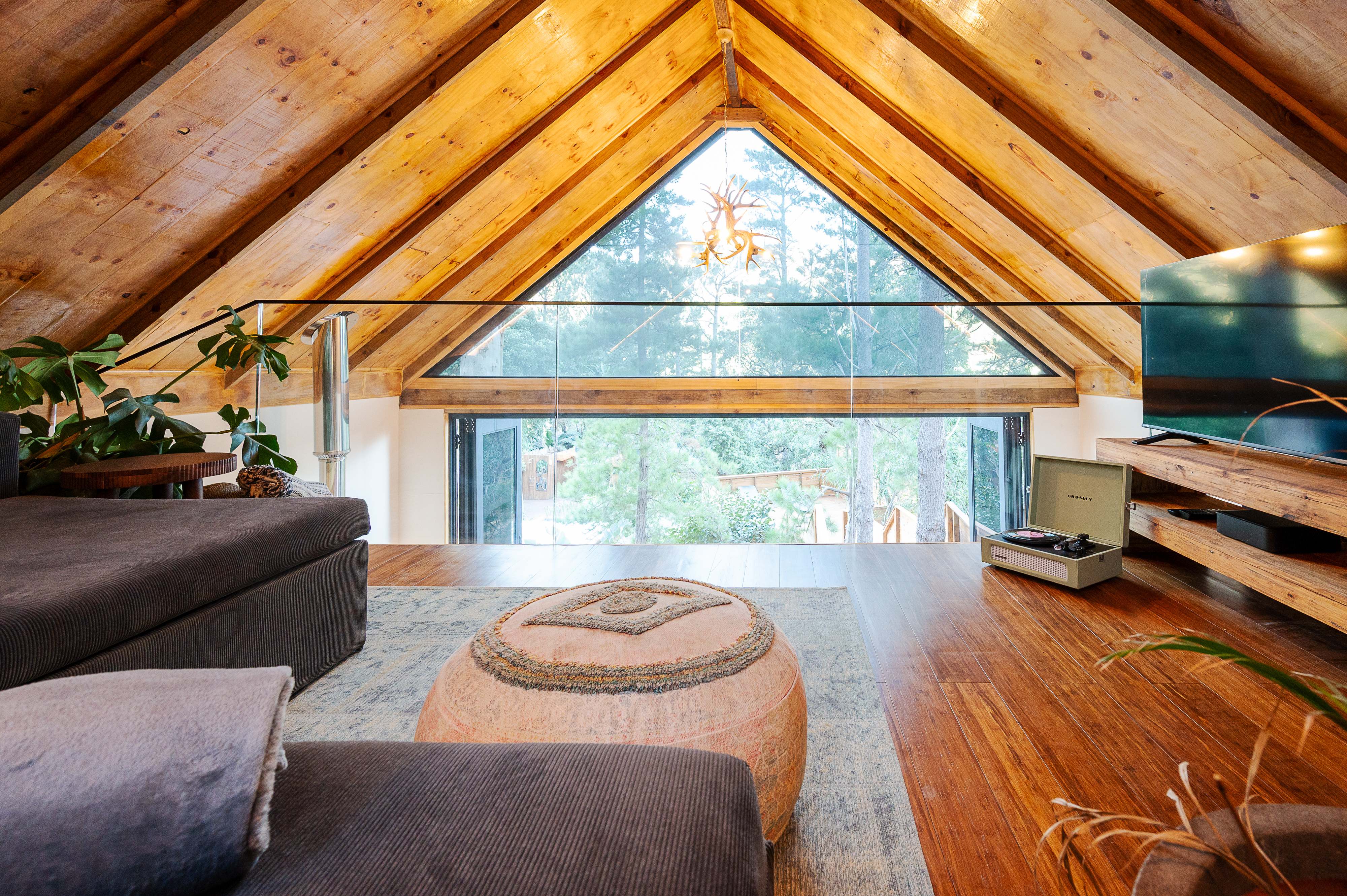 A vaulted timber loft with exposed beams and a gable window over the forest