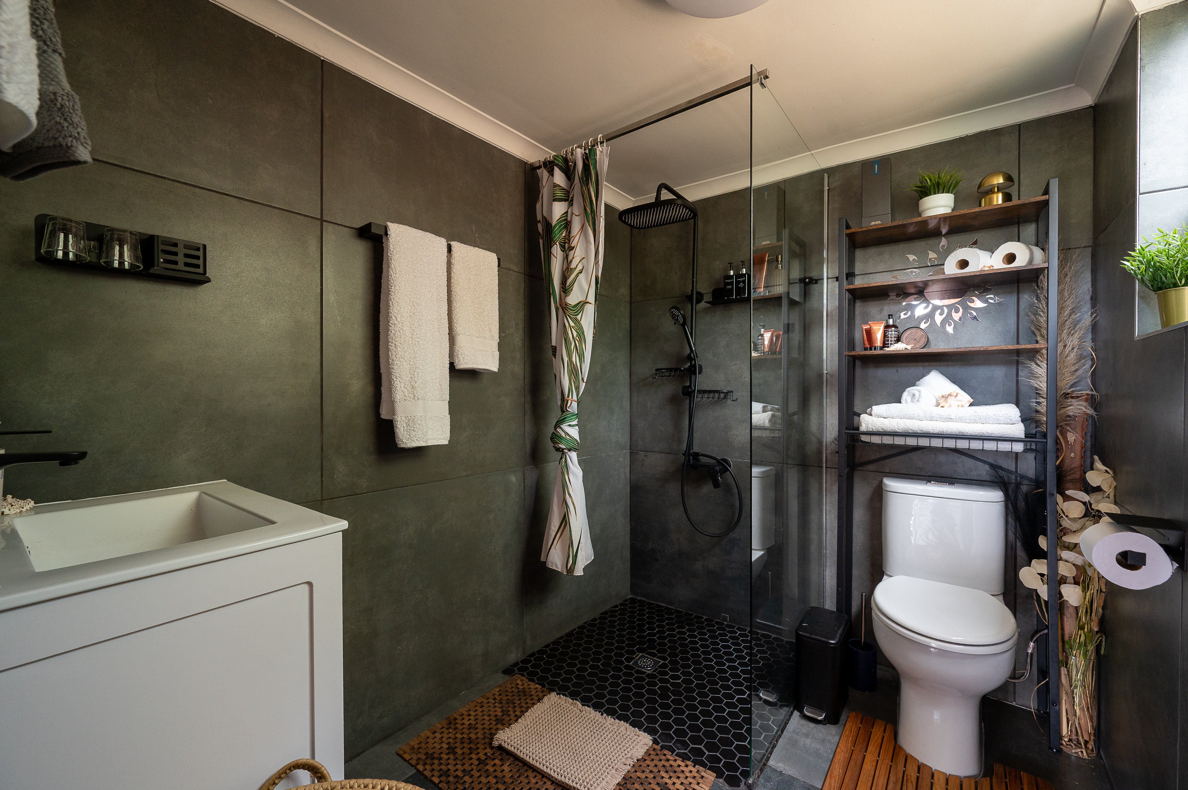 Bathroom with dark green tiled walls and a glass walk in shower with black hexagon floor tiles