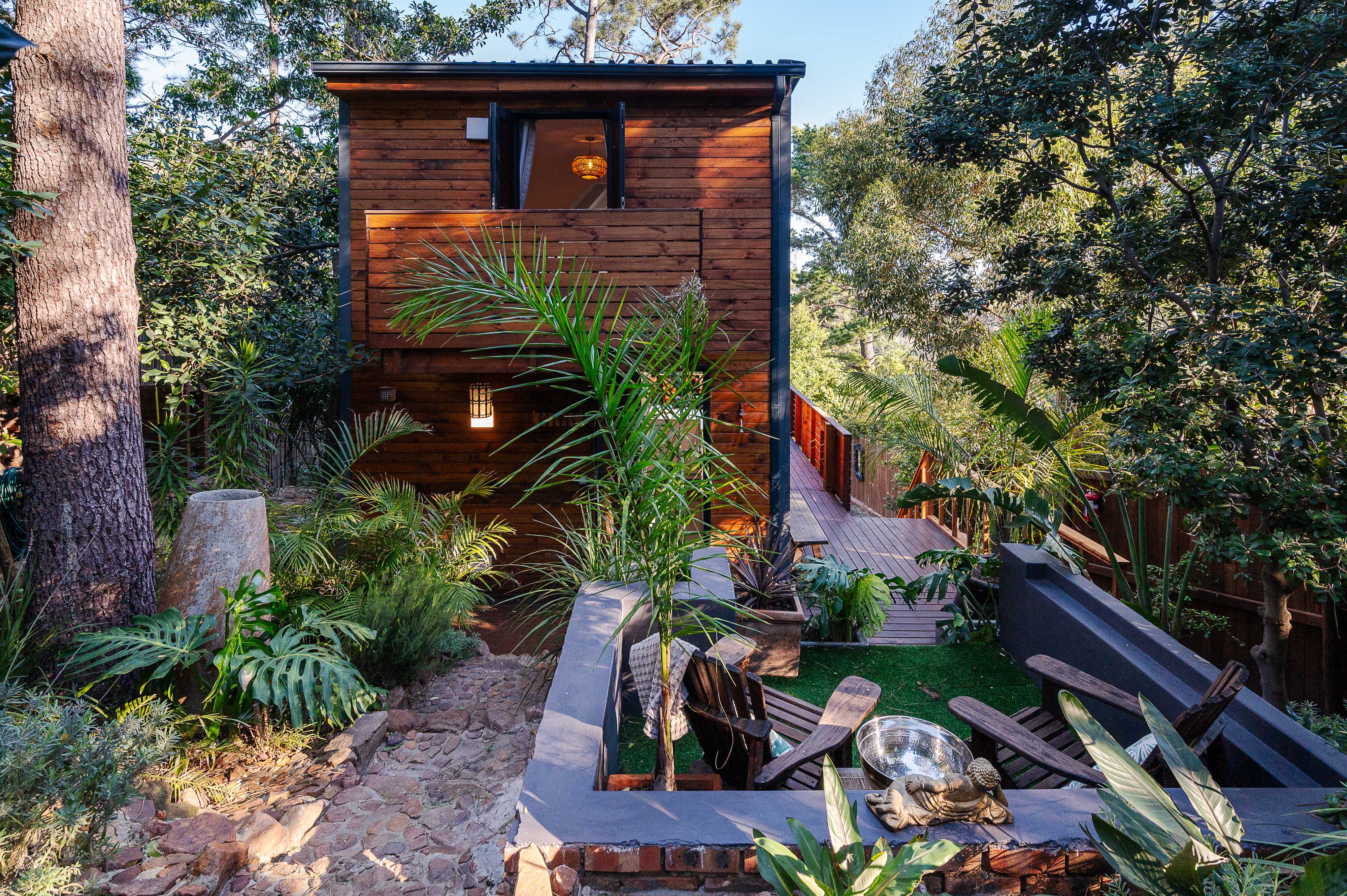 The cabin nestled in a lush forest garden with timber decking and tropical planting