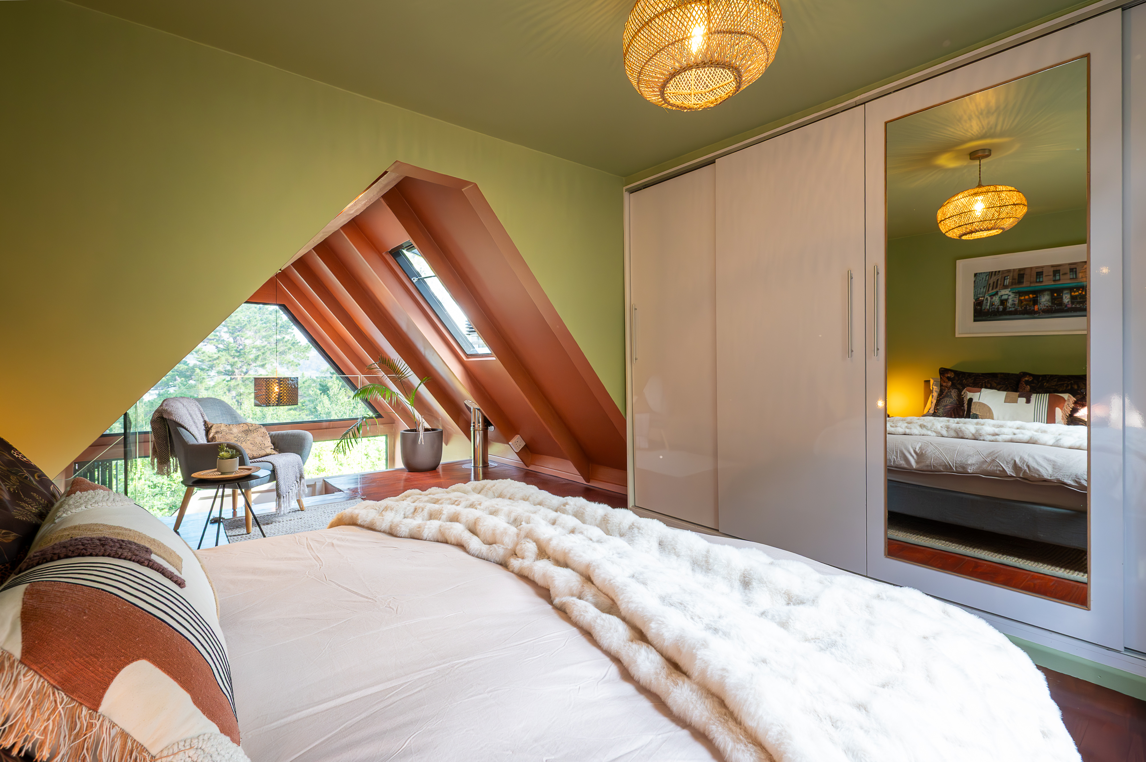 Mezzanine loft bedroom set beneath a triangular gable window with a mirrored wardrobe