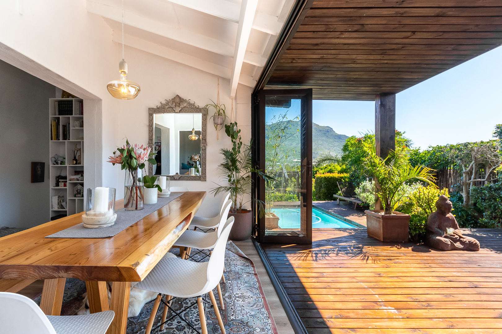 Living and dining space opening onto a timber deck with a pool and mountain views